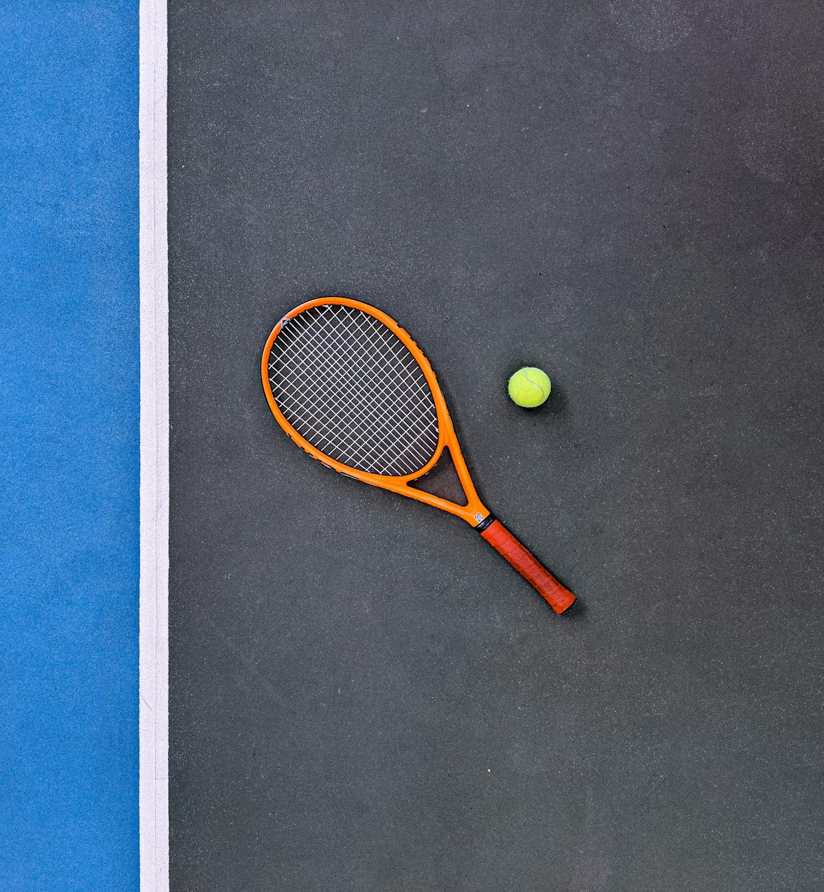 orange tennis racket beside green tennis ball
